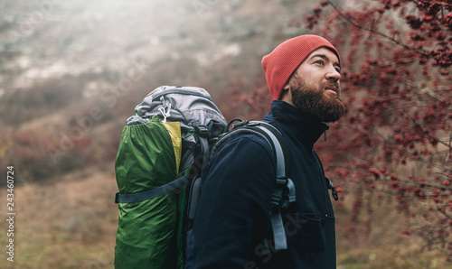 Horizontal portrait of hiker young male hiking in mountains with travel backpack. Traveler man with beard trekking and mountaineering. Travel, people, healthy lifestyle concept