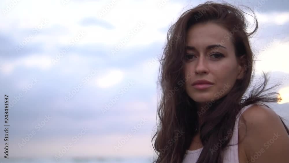 pretty brunette woman posing on the camera near the ocean at sunset pretty brunette woman posing on the camera near the ocean at sunset
