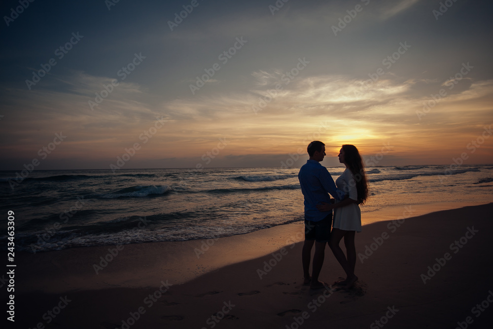 Two young lovers standing on a beach and looking to each other on sunset background.sillhouette couple love