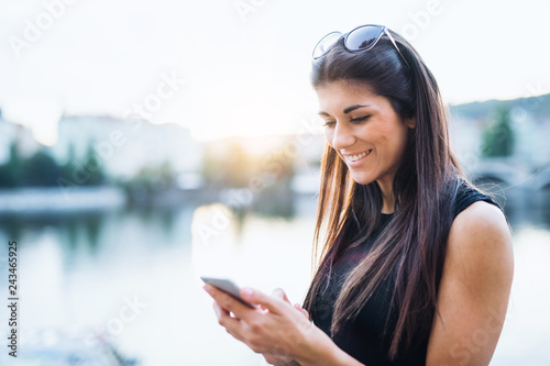 Beautiful woman in black dress standing by a river in city of Prague, text messaging.