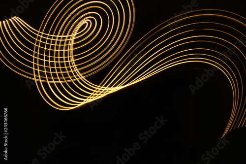 Light painting, long exposure photography, metallic gold yellow color against a black background