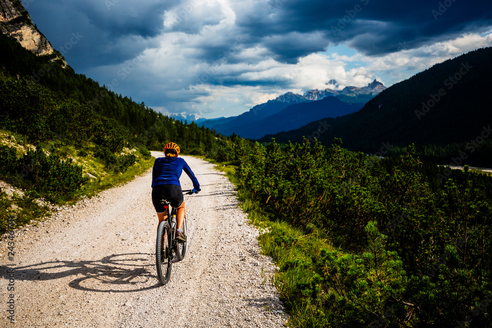 Tourist cycling in Cortina d'Ampezzo, stunning rocky mountains on the background. Woman riding MTB enduro flow trail. South Tyrol province of Italy, Dolomites. Tourist cycling in Cortina d'Ampezzo, stunning rocky mountains on the background. Woman riding MTB enduro flow trail. South Tyrol province of Italy, Dolomites.