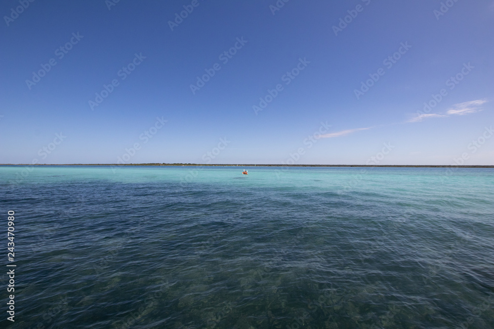 Blue and blue Caribbean sea with crystal clear waters and clear sky. a kayak moves in the distance on the coral reef sea. sports activities at the seaside