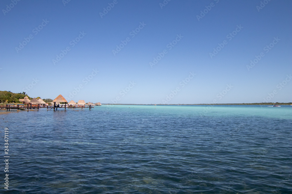 blue and blue Caribbean sea with crystal clear waters and clear sky. a bungalow with a pier in the middle of the lagoon in a coral reef. hotel and rooms by the sea