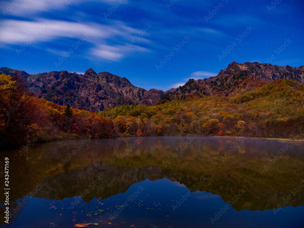 池のほとりで深夜の月明かりで山々を撮影、空には雲と星が輝く、山々は紅葉で色取り取りとなり、手前の池には鏡の様に姿を写し出す。