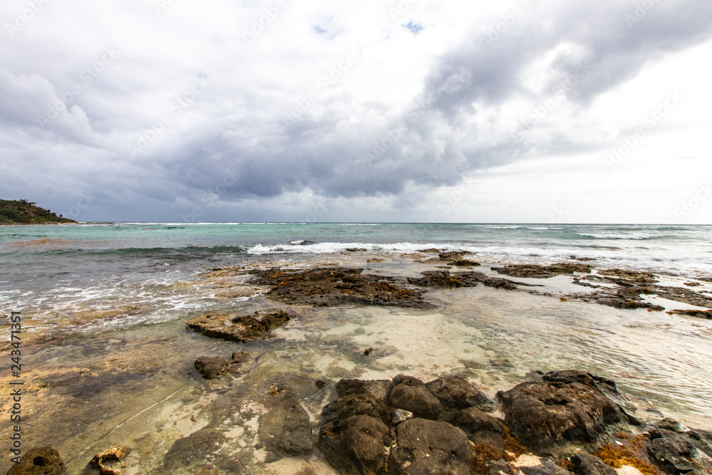 Caribbean bay with rocks, sandy beach and coral reef. clear sea of a coral reef beach with beach and clouds on the horizon and waves crashing on the shore