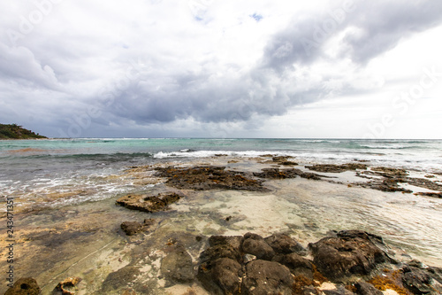 Caribbean bay with rocks, sandy beach and coral reef. clear sea of a coral reef beach with beach and clouds on the horizon and waves crashing on the shore