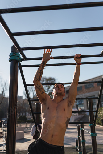 Young athletic guy training on pull up bars in outdoor gym