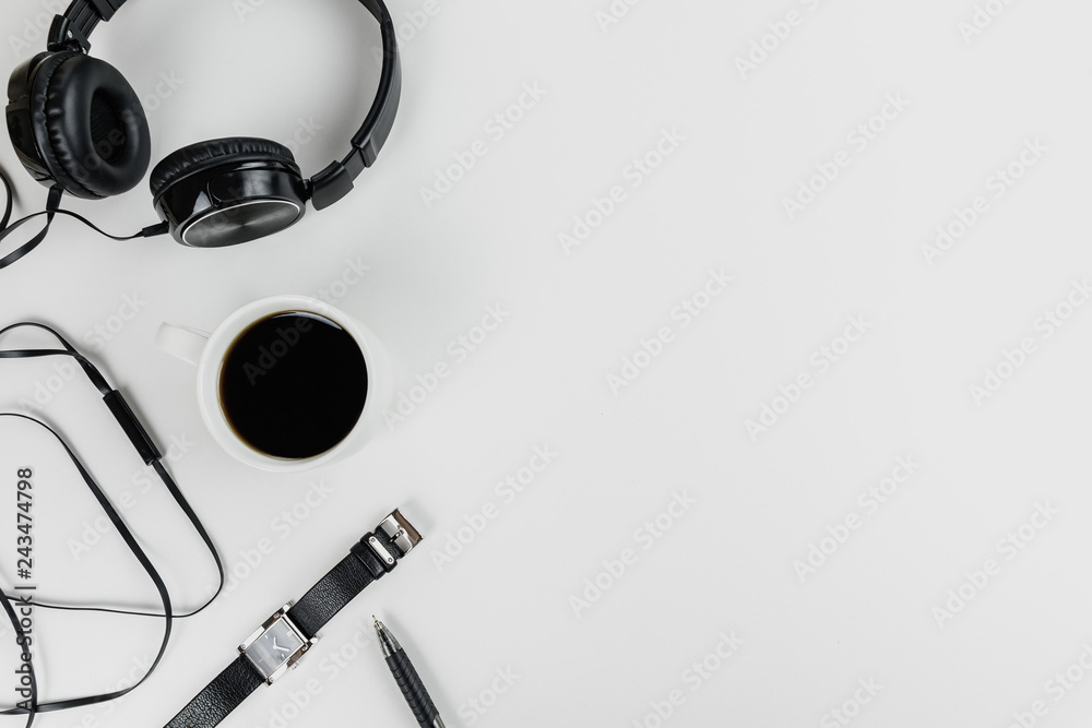 Top view on a freelancer's workspace. White table top with black headphones, watch, pen and cup of coffee. Flat lay with copy space. - obrazy, fototapety, plakaty 