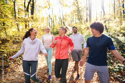 Small group of runners dressed in sportswear talking and walking through woods in autumn.