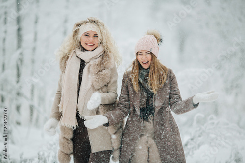 Photo of two blondes throwing snow on walk in winter forest