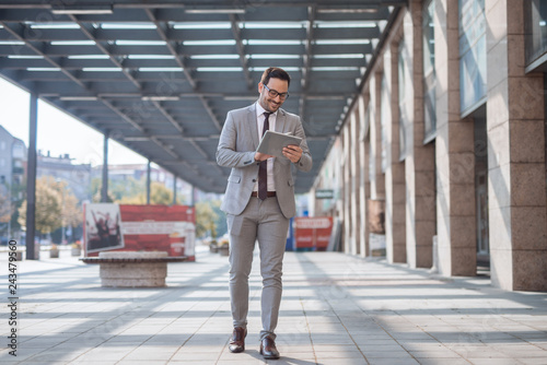 Businessman walking on the street and using tablet to check an e-mail. In background business center exteriour. photo