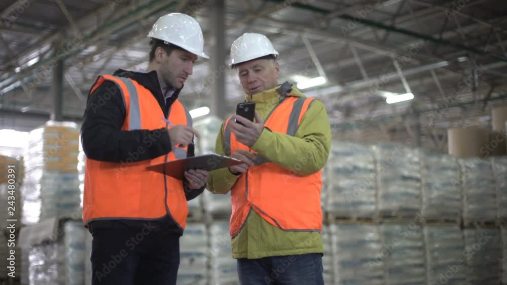 Two businessman discussing the new project, using cellphone in warehouse. Two businessman discussing the new project, using cellphone in warehouse.