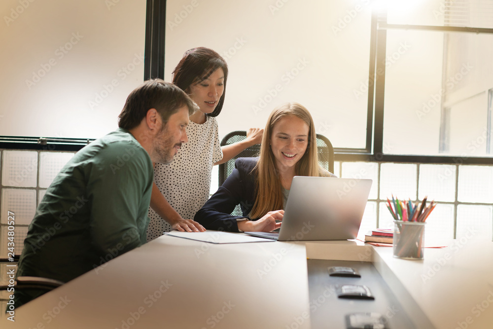 Group of three co workers looking over computer in modern workplace Group of three co workers looking over computer in modern workplace