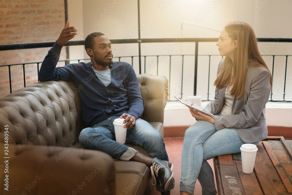 Co workers casually discussing ideas on sofa in modern workplace Co workers casually discussing ideas on sofa in modern workplace