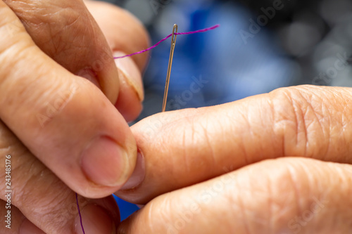 Senior woman s hands trying to thread a needle  Purple colour roll of thread  Close up   Macro shot  Selective focus  Blurred and bokeh background  Tailor  Needlework concept