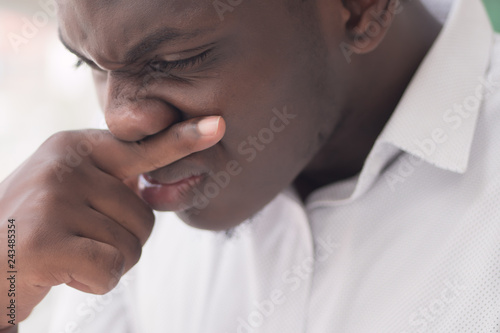Sick African man with runny nose; Portrait of ill black man suffering from runny nose due to cold; flu; allergy; polluted air; dust; smog; air pollution sickness concept; African young adult man model