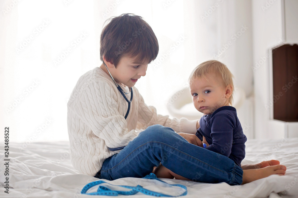 Little toddler boy, playing with his little brother to doctor at home in bedroom Little toddler boy, playing with his little brother to doctor at home in bedroom