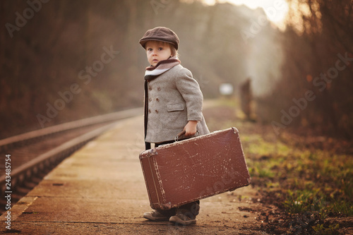 Adorable boy on a railway station, waiting for the train with suitcase and teddy bear photo