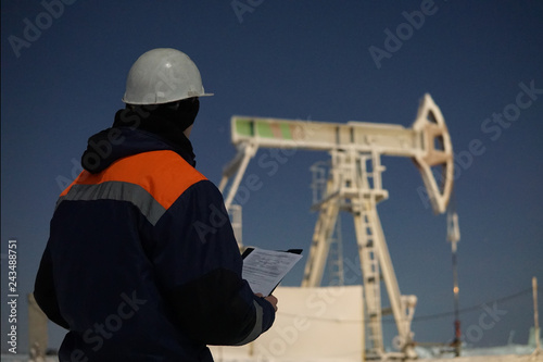 Oil worker check oil pump. Oil Drill, field pump jack with snow storm and worker. Fossil Energy Resource Concept.