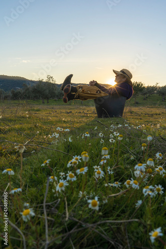 Woman with straw hat sitting in the field at sunset