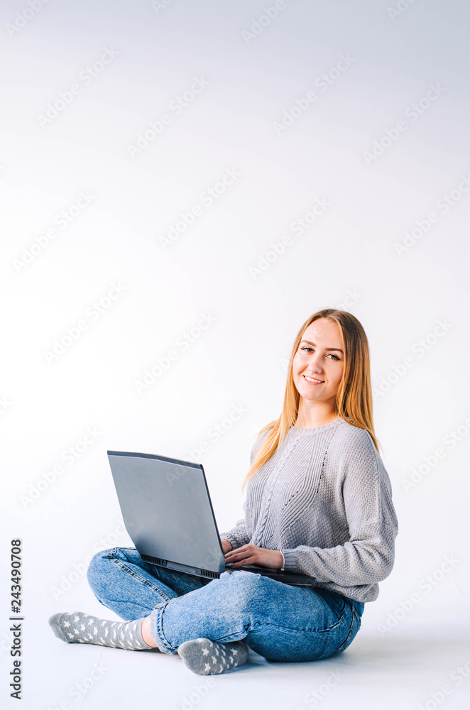 Naklejka premium The girl sits on a light background and works behind a laptop.