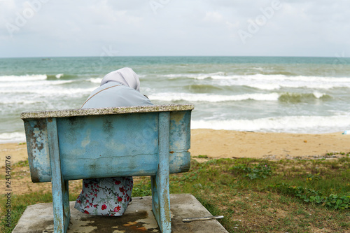 Muslim young mother wearing hijab with cute little boy relaxing at a bench by the beach - Image 