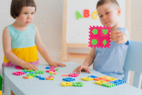 A boy and a girl collect a soft puzzle at the table. Brother and sister have fun playing together in the room.