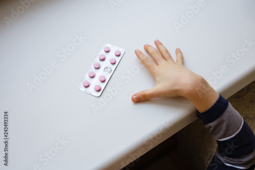 Child takes pack of pills. Dangerous situation. A small child curious about a prescription drug container illustrating the importance of drug safety and parental supervision and communication.