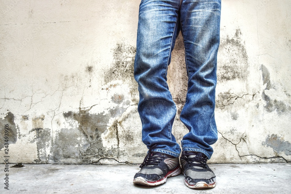 Fashion jeans men wearing old shoes standing close to the background, old walls with cracks and black stains in the vintage background.
