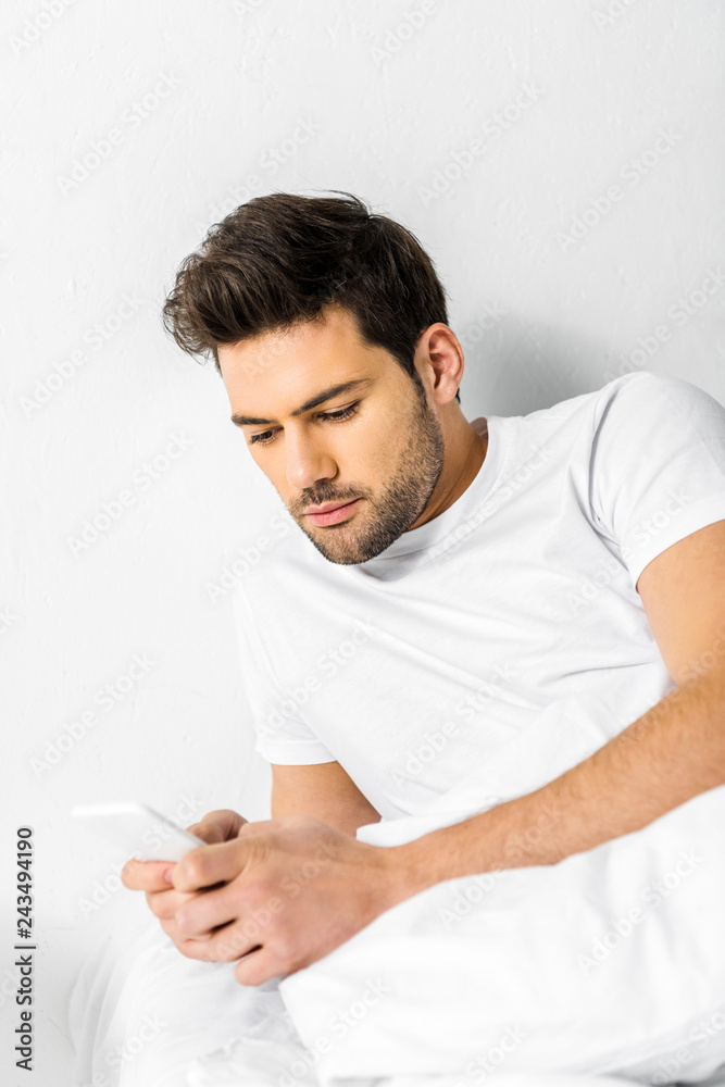 handsome man using smartphone while resting in bed in the morning handsome man using smartphone while resting in bed in the morning