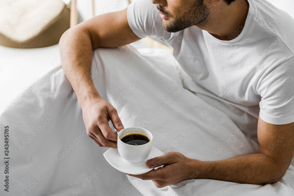 cropped view of man holding cup of coffee while sitting in bed