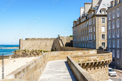 Fototapeta View over the rampart walk of the old town of Saint-Malo in Brittany, France, above the Môle beach on a sunny day, with the bastion of Holland in the background
