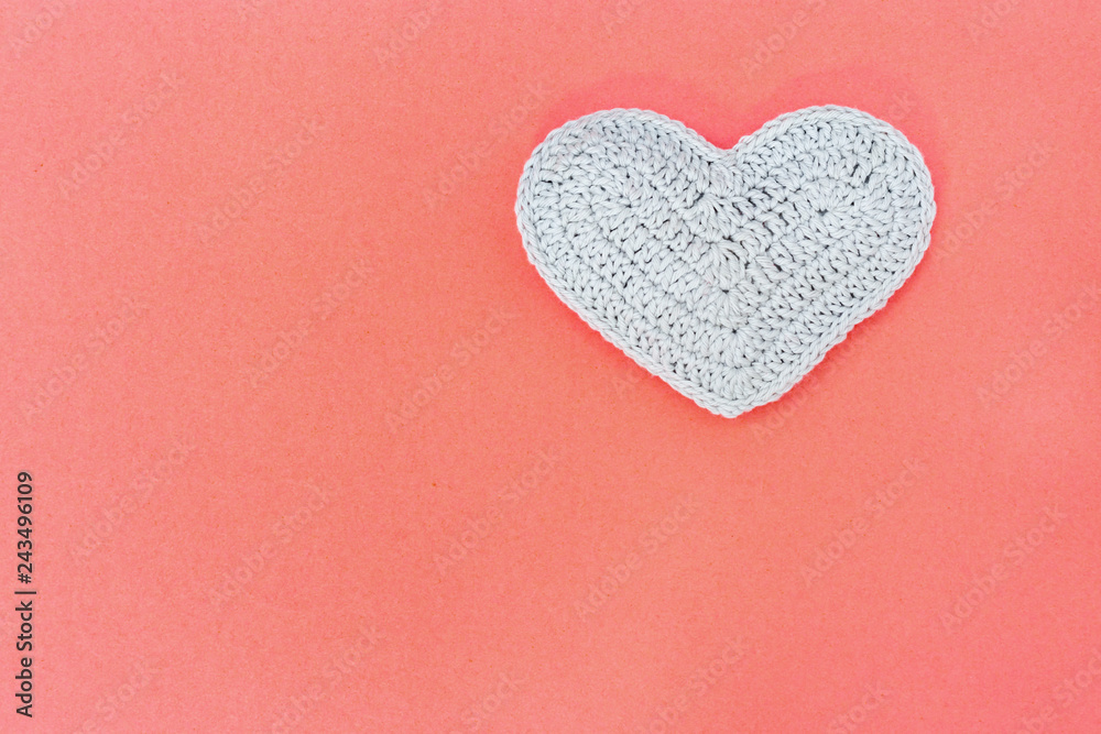Handmade gray knitted heart on paper background with copy space for text. Valentine’s day background concept.