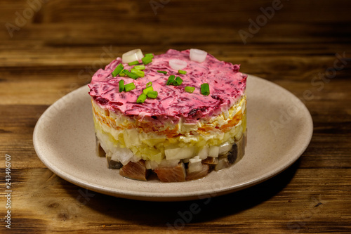 Traditional russian salad "Herring under a fur coat" (shuba) on wooden table. Layered salad with herring, beets, carrots, onions, potatoes and eggs