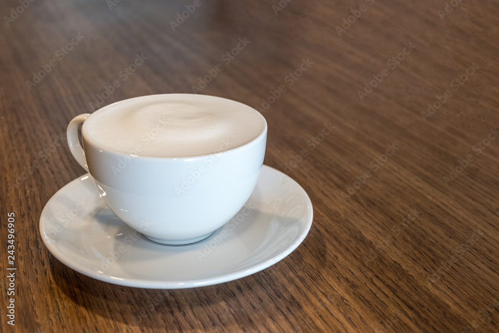Fototapeta premium Close up a cup of coffee with milk froth on wooden table background