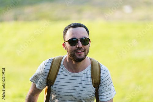Hiking man portrait with backpack walking in nature. Caucasian man smiling happy with forest in background during summer trip
