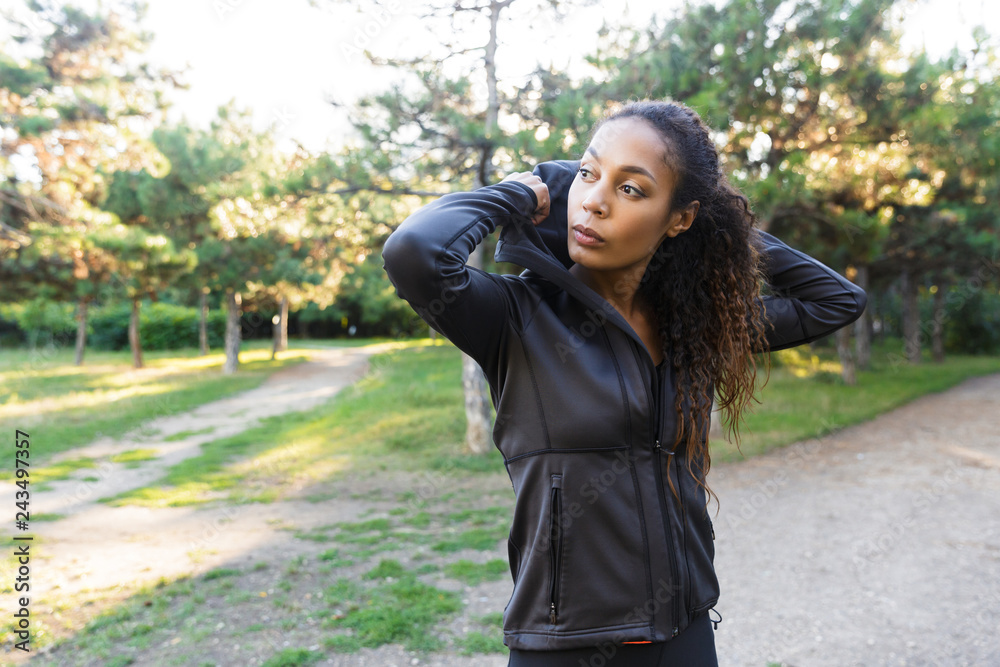 Image of brunette woman 20s wearing black tracksuit, walking through green park Image of brunette woman 20s wearing black tracksuit, walking through green park