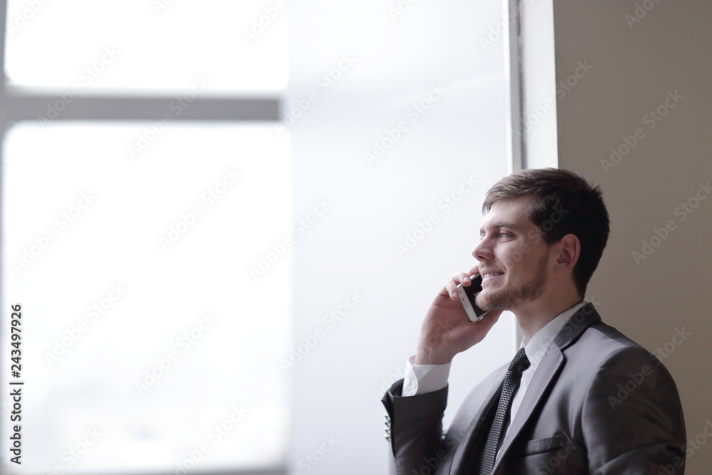 close up.businessman talking on smartphone while standing near an office window close up.businessman talking on smartphone while standing near an office window