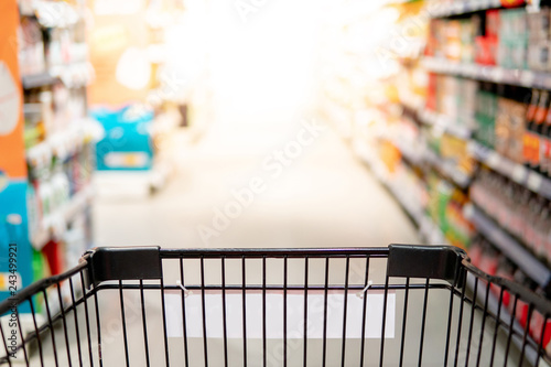 Empty black shopping cart or shopping trolley in aisle of supermarket or grocery store. Buying goods concept.