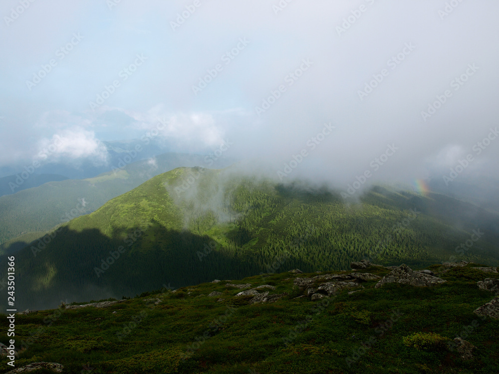 Picturesque landscape of Carpathian mountains with rainbow over them.  Heaven kitchen prepares rainy whether in summer in mountains. Eastern Carpathians, Ukraine