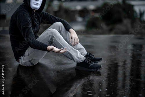 Reflection of mystery hoodie man in white mask sitting in the rain on rooftop of abandoned building. Bipolar disorder or Major depressive disorder. Depression concept
