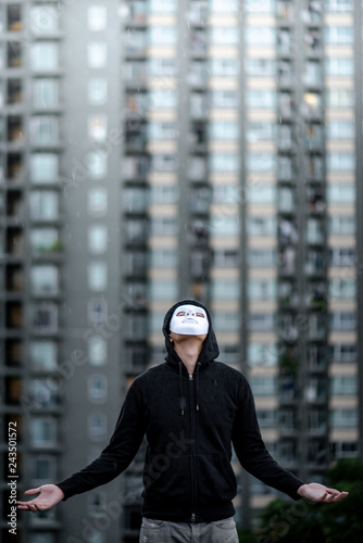 Mystery hoodie man in white mask standing in the rain looking up at the sky on rooftop of abandoned building. Bipolar disorder or Major depressive disorder. Depression concept