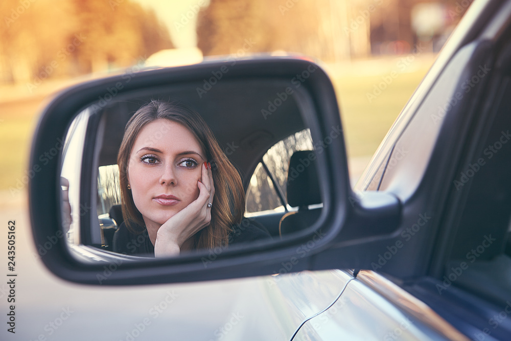 Rear view of attractive young woman in casual wear looking in rear-view mirror in her car