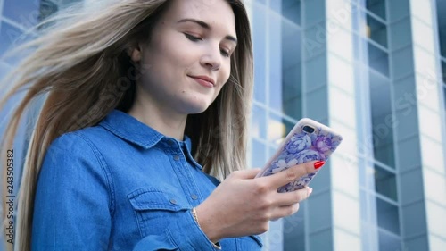 Beautiful lady using her mobile phone, smarthone, texting in front of a modern urban city architecture