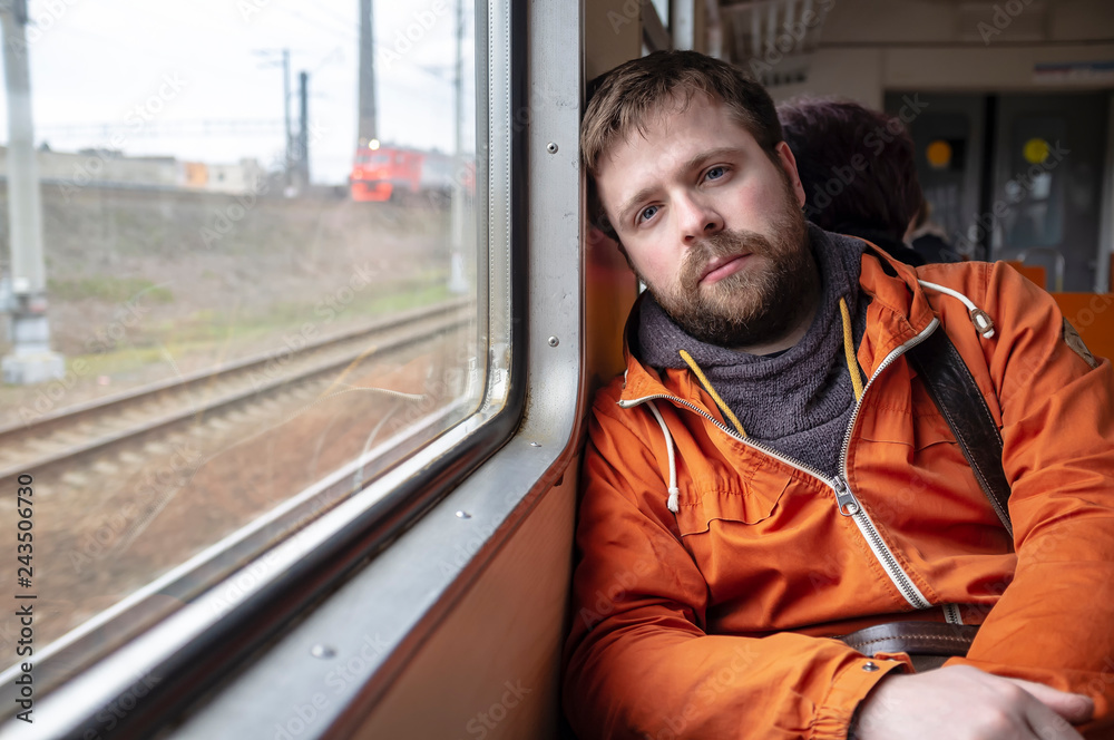 A handsome, bearded man rides the train, leaning against the wall near the window for fatigue. Close-up. A handsome, bearded man rides the train, leaning against the wall near the window for fatigue. Close-up.