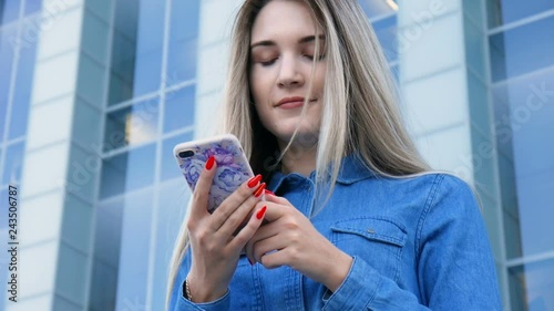Beautiful lady using her mobile phone, smarthone, texting in front of a modern urban city architecture