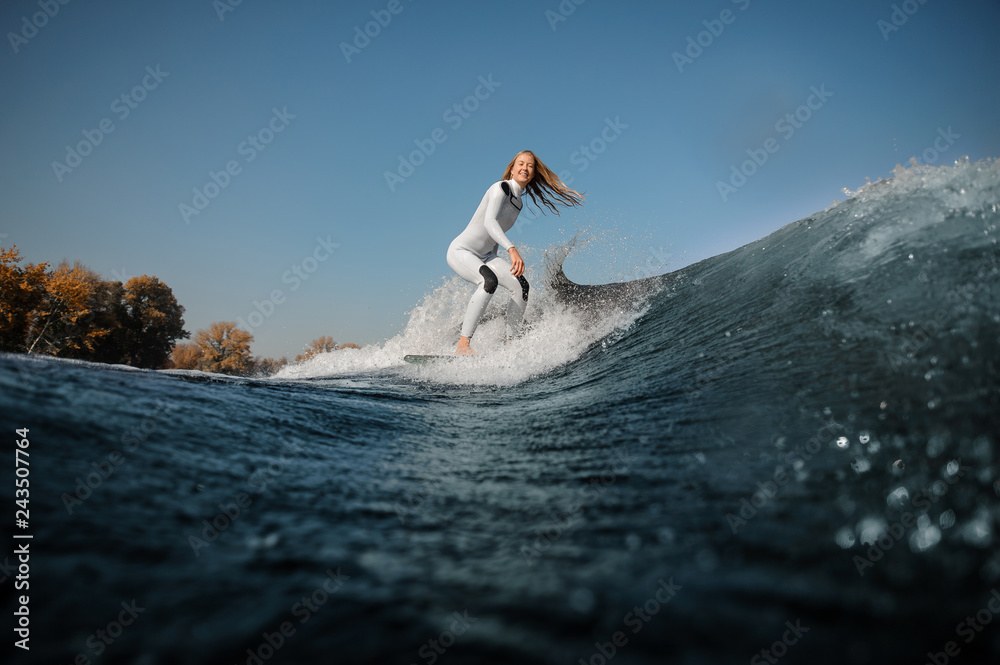 Smiling blonde girl riding on the wakeboard on the bending knees