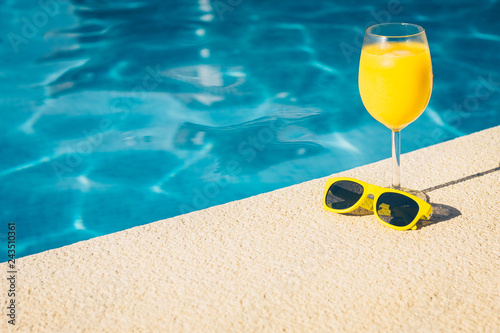 Resort vacation concept - close-up sunglasses and glass of juice on a bright sunny day by the pool - copy space