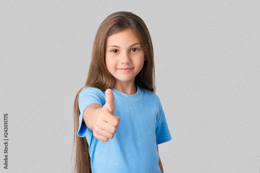 Smiling girl dressed in blue t-shirt showing big finger and approving somebody's work against a grey background Smiling girl dressed in blue t-shirt showing big finger and approving somebody's work against a grey background